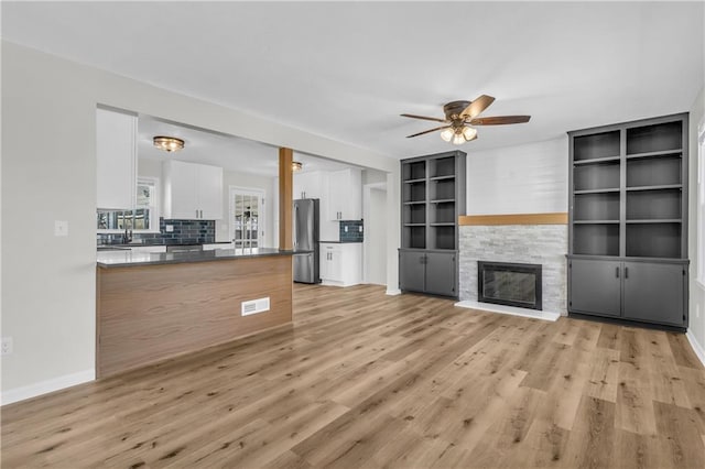 unfurnished living room with ceiling fan, a fireplace, and light hardwood / wood-style floors