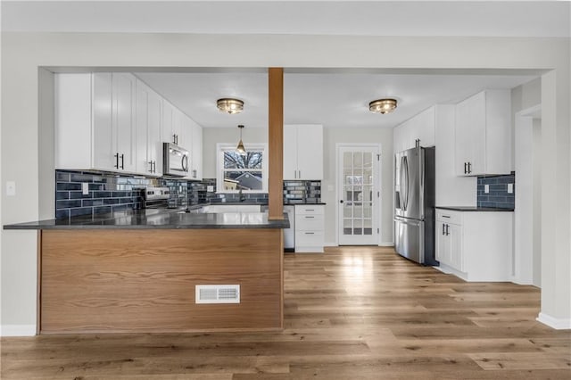 kitchen with appliances with stainless steel finishes, white cabinets, decorative light fixtures, kitchen peninsula, and light wood-type flooring