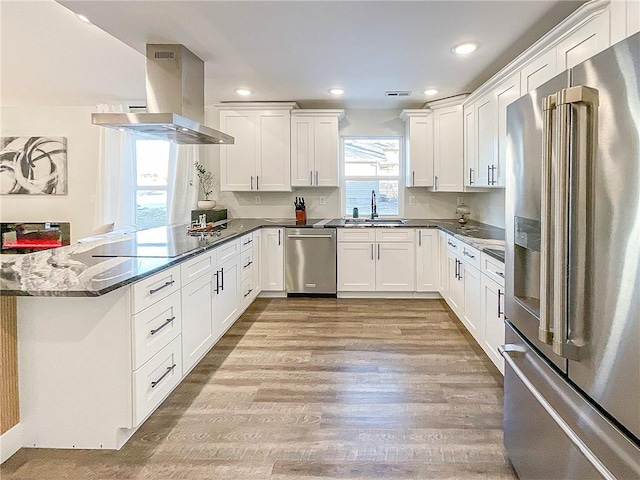 kitchen featuring sink, dark stone countertops, white cabinets, island exhaust hood, and stainless steel appliances