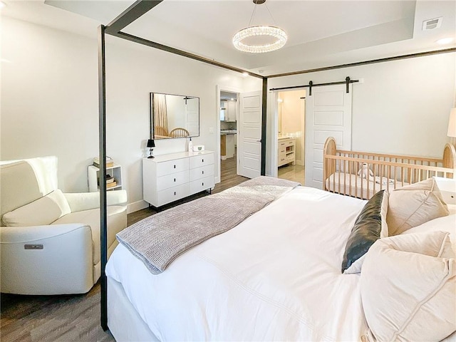 bedroom featuring wood-type flooring, a barn door, and a raised ceiling