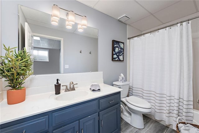 full bathroom with shower / bathtub combination with curtain, hardwood / wood-style floors, vanity, a drop ceiling, and toilet