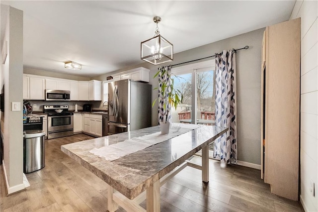 kitchen featuring stainless steel appliances, white cabinetry, light hardwood / wood-style floors, and decorative light fixtures