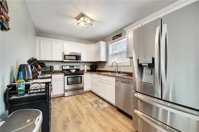 kitchen with appliances with stainless steel finishes, sink, light hardwood / wood-style flooring, and white cabinets