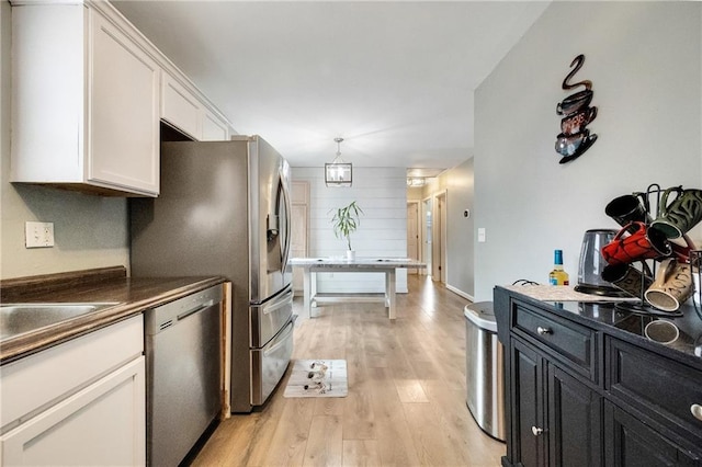 kitchen with white cabinetry, an inviting chandelier, stainless steel dishwasher, pendant lighting, and light hardwood / wood-style floors