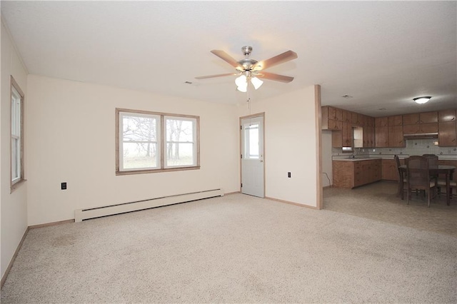unfurnished living room featuring a baseboard heating unit, a sink, ceiling fan, and baseboards