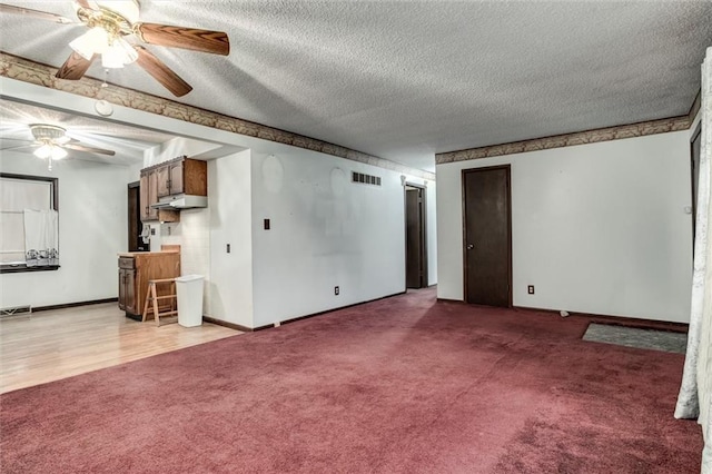 unfurnished living room featuring a textured ceiling, ceiling fan, carpet floors, visible vents, and baseboards