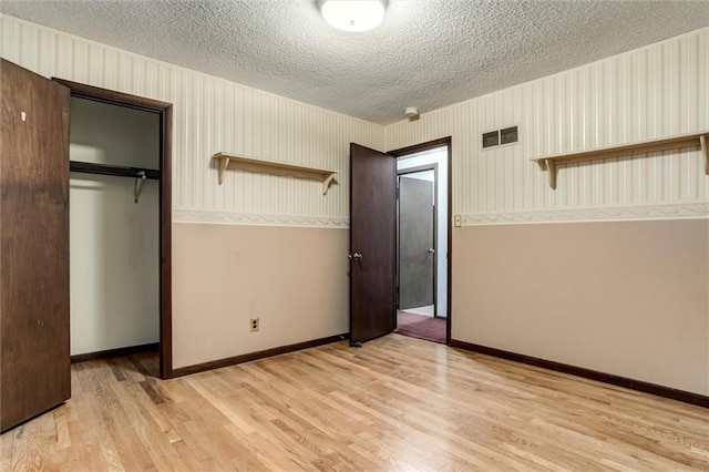 unfurnished bedroom with light wood finished floors, a closet, visible vents, a textured ceiling, and baseboards