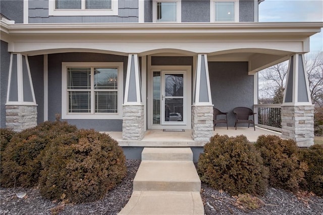 view of exterior entry with stone siding, covered porch, and stucco siding