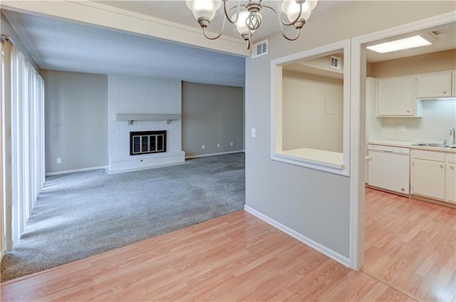 unfurnished living room with sink, an inviting chandelier, a textured ceiling, a brick fireplace, and light hardwood / wood-style flooring