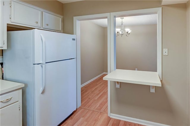 kitchen featuring white cabinetry, decorative light fixtures, a chandelier, light hardwood / wood-style flooring, and white fridge