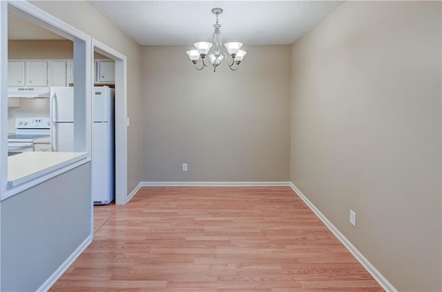 unfurnished dining area with light wood-type flooring, a textured ceiling, and a notable chandelier