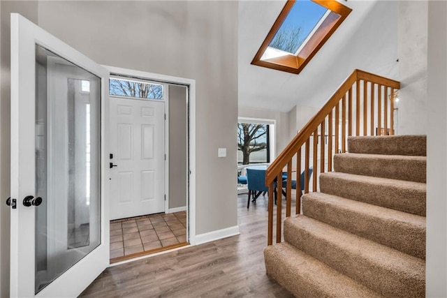 entryway featuring high vaulted ceiling, a skylight, wood finished floors, baseboards, and stairway