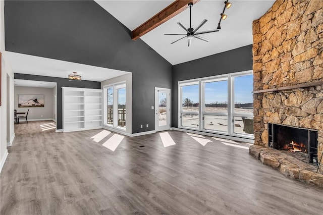 unfurnished living room featuring a stone fireplace, beamed ceiling, wood finished floors, and baseboards