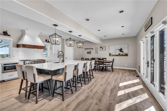 kitchen featuring decorative light fixtures, a center island with sink, light countertops, custom range hood, and a sink