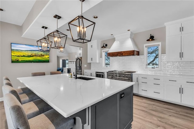 kitchen with white cabinets, hanging light fixtures, an island with sink, and custom exhaust hood