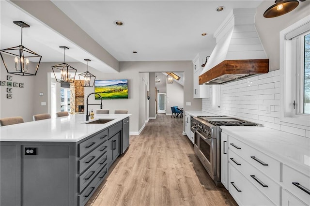 kitchen with stainless steel appliances, white cabinetry, hanging light fixtures, custom exhaust hood, and an island with sink