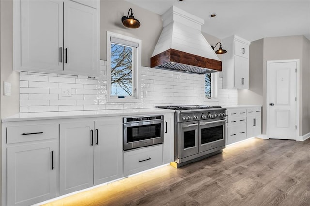 kitchen featuring white cabinets, double oven range, light countertops, and premium range hood