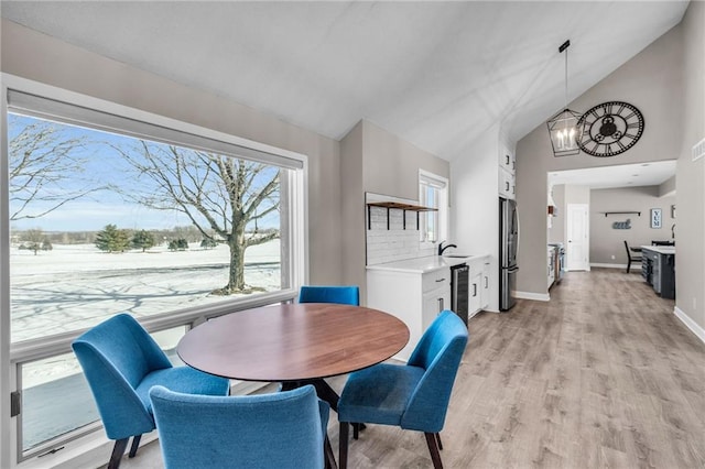 dining space featuring high vaulted ceiling, light wood-type flooring, a notable chandelier, and baseboards