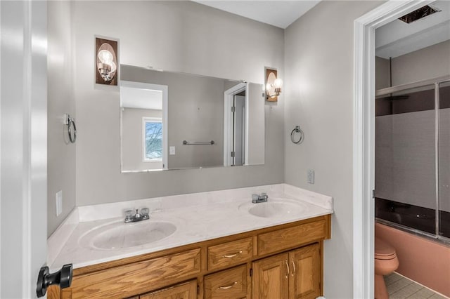 bathroom featuring double vanity, shower / bath combination with glass door, a sink, and toilet