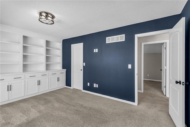 interior space featuring baseboards, visible vents, a textured ceiling, and light colored carpet