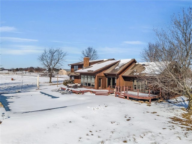 snow covered rear of property with a chimney and a deck