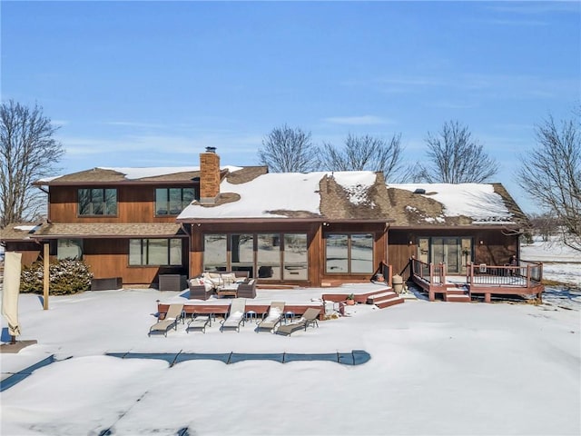 snow covered back of property with a chimney and a wooden deck