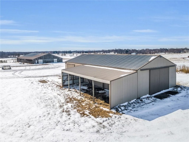 snow covered structure featuring a carport and an outbuilding