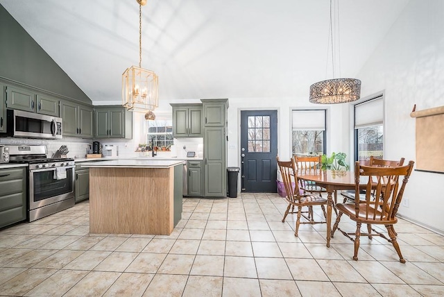 kitchen with decorative light fixtures, appliances with stainless steel finishes, a kitchen island, a notable chandelier, and a healthy amount of sunlight