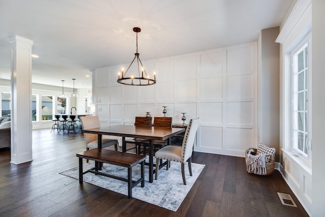 dining space featuring an inviting chandelier, decorative columns, and dark hardwood / wood-style floors