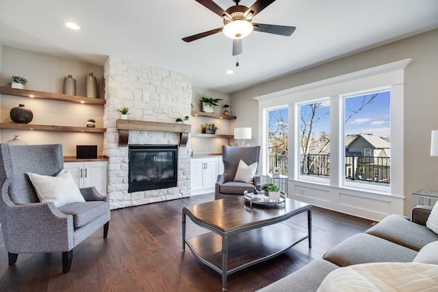 living room featuring ceiling fan, a stone fireplace, and dark hardwood / wood-style flooring