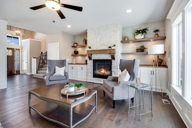 living room featuring dark hardwood / wood-style flooring, a stone fireplace, a wealth of natural light, and ceiling fan with notable chandelier