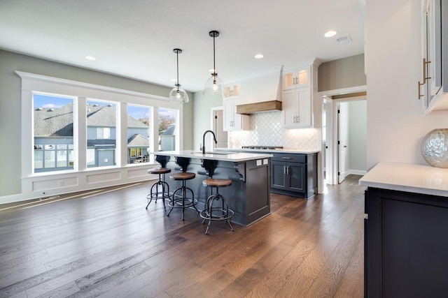 kitchen with a breakfast bar area, white cabinetry, tasteful backsplash, hanging light fixtures, and custom range hood