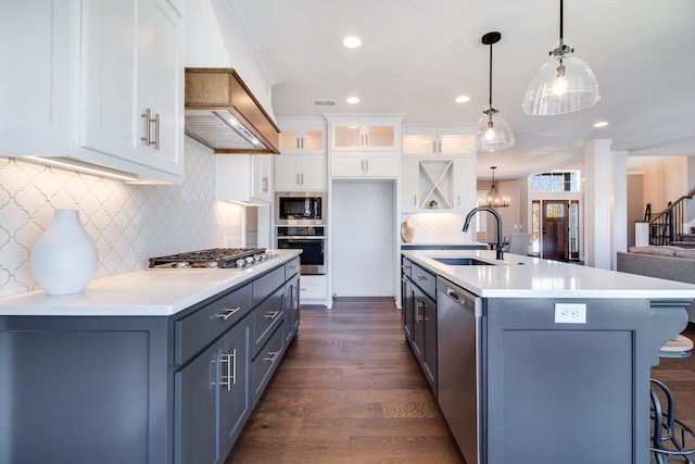 kitchen with sink, white cabinetry, hanging light fixtures, appliances with stainless steel finishes, and an island with sink