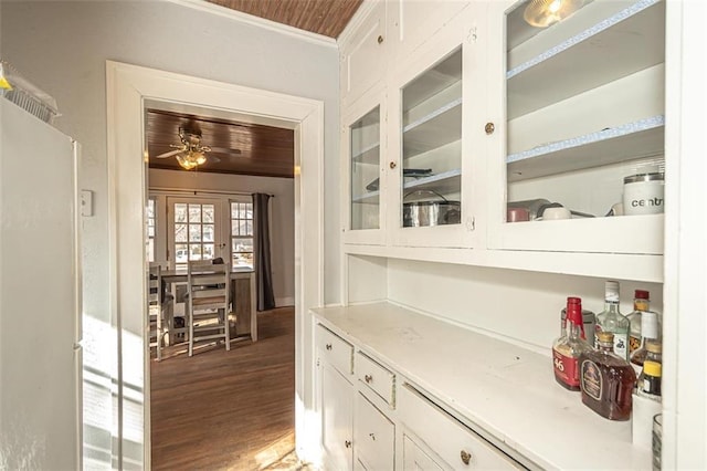 bar featuring white cabinets, white fridge, ceiling fan, crown molding, and dark wood-type flooring