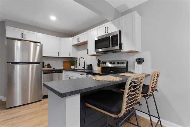 kitchen featuring appliances with stainless steel finishes, white cabinetry, backsplash, a kitchen bar, and light hardwood / wood-style flooring