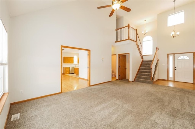 unfurnished living room featuring a towering ceiling, plenty of natural light, light colored carpet, and ceiling fan with notable chandelier