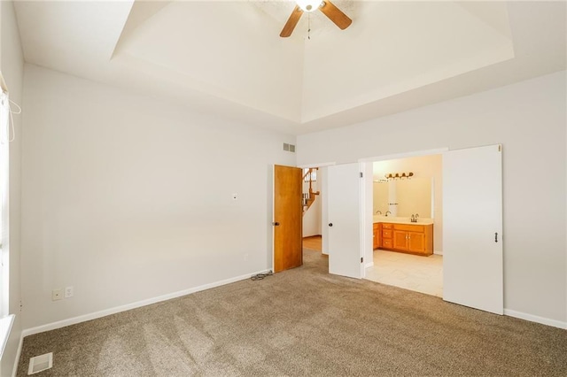 unfurnished bedroom featuring a tray ceiling, light colored carpet, ensuite bathroom, and a high ceiling