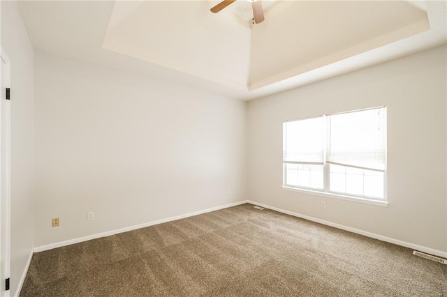 empty room featuring a raised ceiling, ceiling fan, and carpet