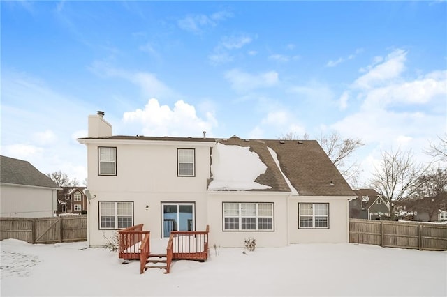 snow covered back of property with a wooden deck