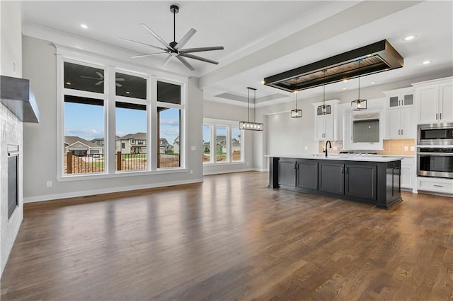 kitchen featuring pendant lighting, a kitchen island with sink, stainless steel appliances, white cabinets, and a raised ceiling