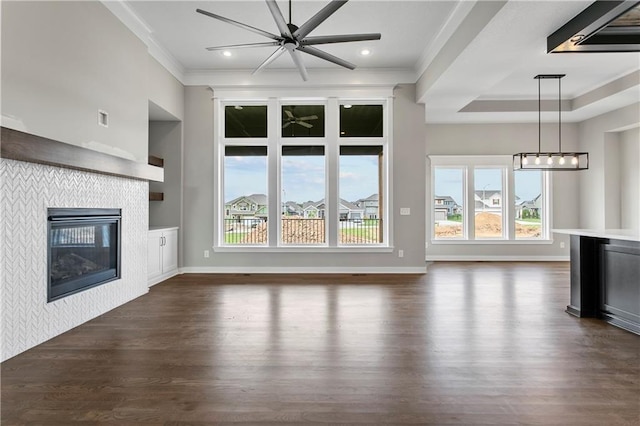 unfurnished living room featuring crown molding, a tray ceiling, dark hardwood / wood-style floors, and a tile fireplace