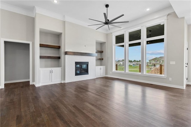 unfurnished living room with built in shelves, dark wood-type flooring, ornamental molding, a tile fireplace, and ceiling fan