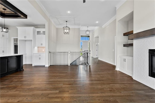 unfurnished living room with dark wood-type flooring, crown molding, and a notable chandelier