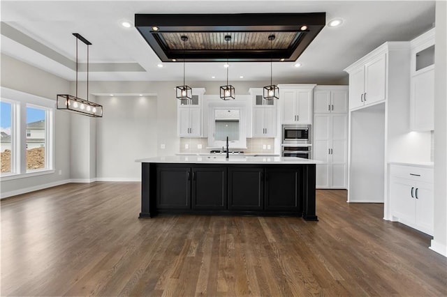 kitchen featuring white cabinetry, appliances with stainless steel finishes, an island with sink, and hanging light fixtures