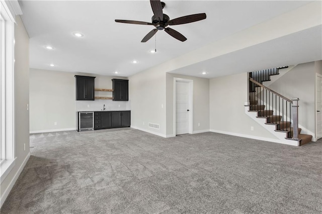 unfurnished living room featuring ceiling fan, bar, beverage cooler, and dark colored carpet