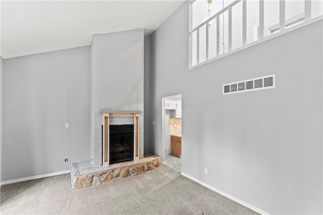 unfurnished living room featuring carpet floors, visible vents, a fireplace with raised hearth, and baseboards