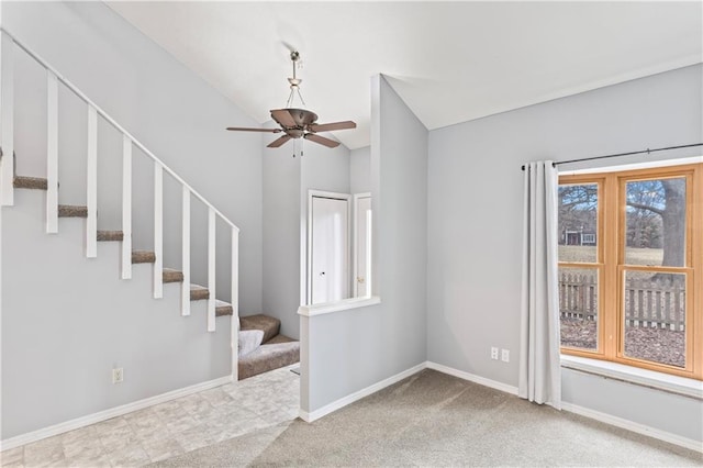 carpeted empty room featuring lofted ceiling, baseboards, stairway, and ceiling fan