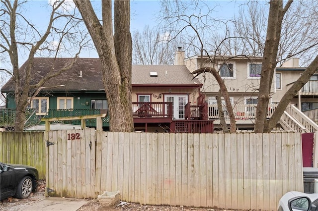 back of house with a fenced front yard, a chimney, a deck, and a shingled roof