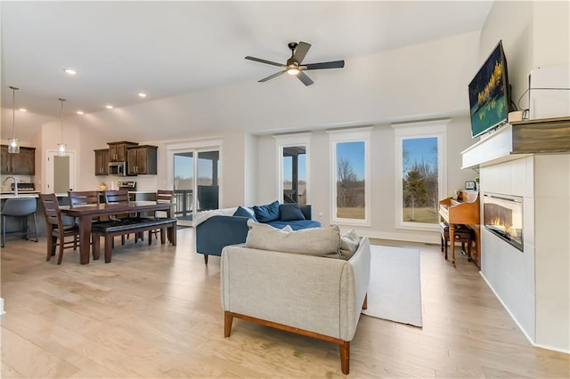 living room with ceiling fan, lofted ceiling, a fireplace, and light hardwood / wood-style floors