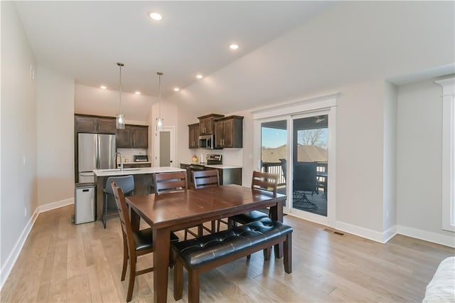 dining space featuring sink, vaulted ceiling, and light wood-type flooring